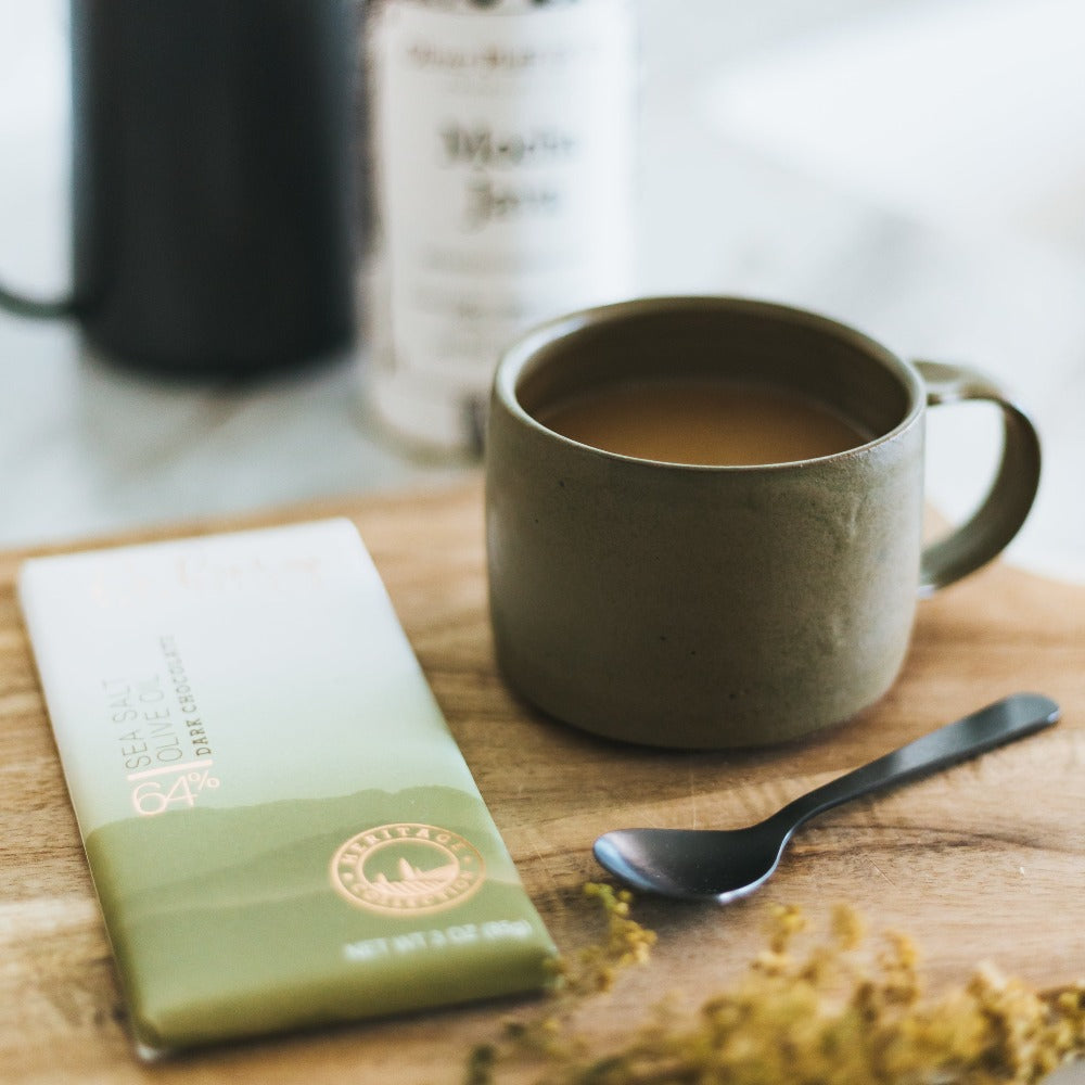 Up close picture of the green coffee mug, dark chocolate bar and black stainless steel coffee spoon.