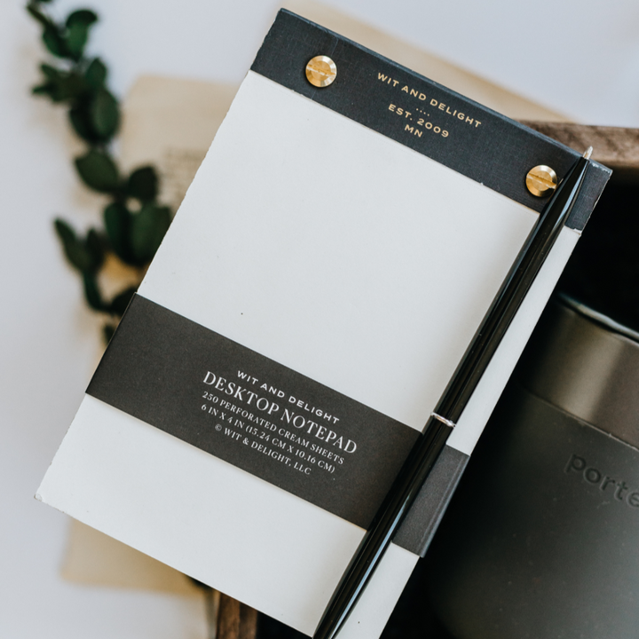 Notepad with black and gold design on a white surface with a plant in the background